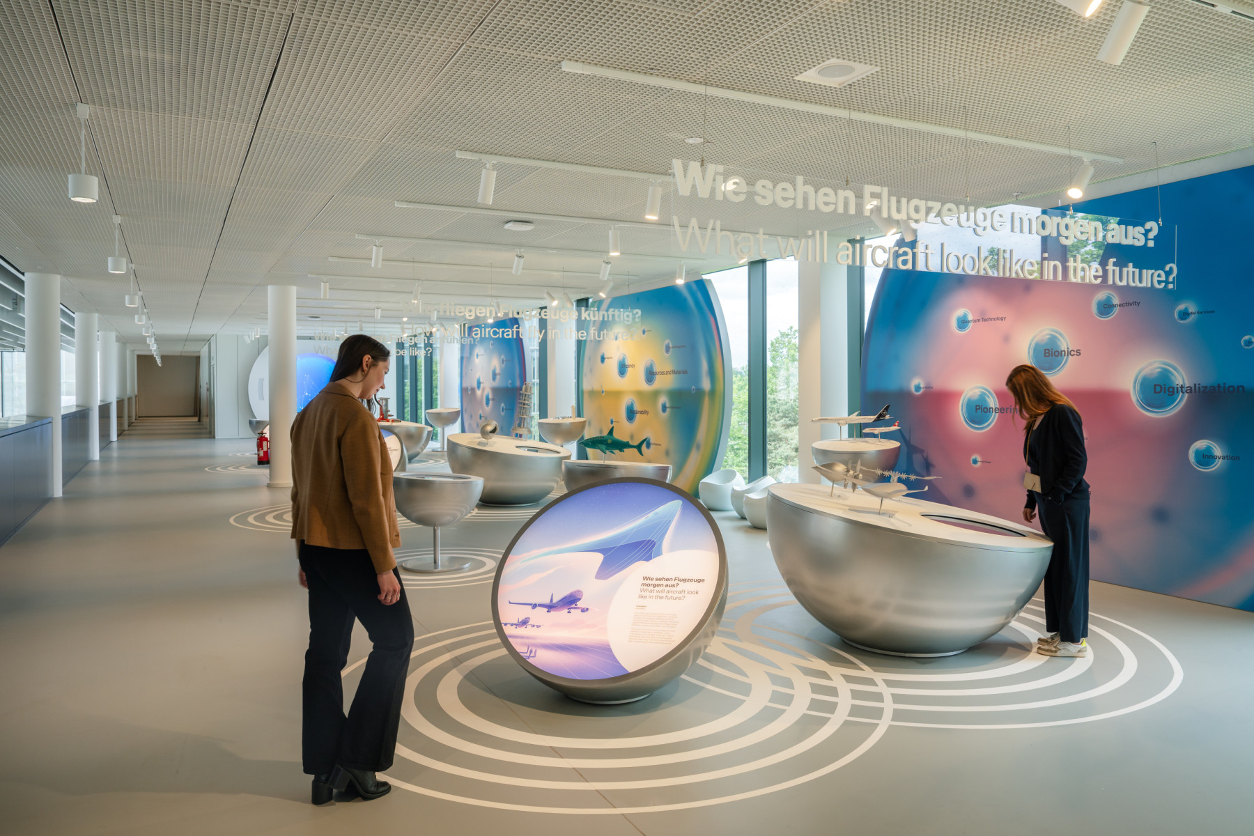 Room with sign 'what will aircraft look like in the future' with two people standing at information boards with small model aircraft and interactive touch elements