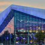 The outside of Hanger One at night with the glass building lit up and a sign reading Lufthansa Group Hanger One