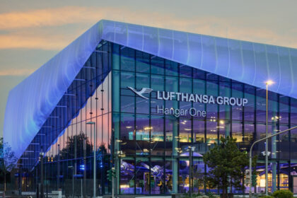 The outside of Hanger One at night with the glass building lit up and a sign reading Lufthansa Group Hanger One