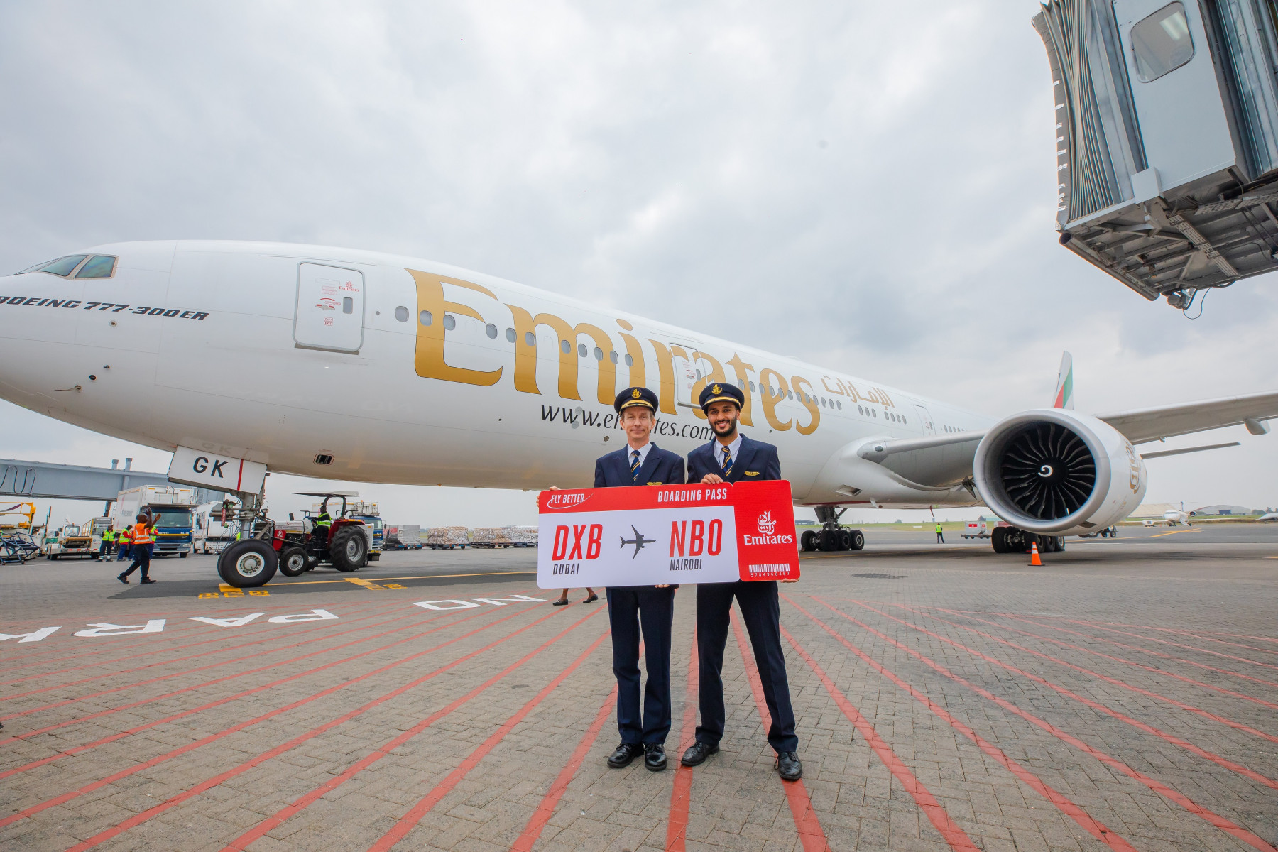 Two pilots in blue uniforms standing in front of an Emirates flight on the runway