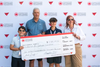 People holding a large cheque in front of Air Canada signage showing $1.5 million raised. Two adults and two children with Air Canada Foundation lanyards.