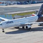 Image shows a Lufthansa Airbus A340-300 aircraft with white and blue livery, grounded at an airport during the day