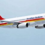 An Aerolinee Siciliane aircraft flying in the blue sky. White, red and yellow livery.