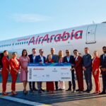 An image of Gatwick and Air Arabia employees holding a large boarding pass standing in front of a Air Arabia aircraft