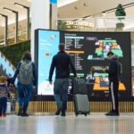 Image shows London Gatwick Airport with screens and passengers with baggage