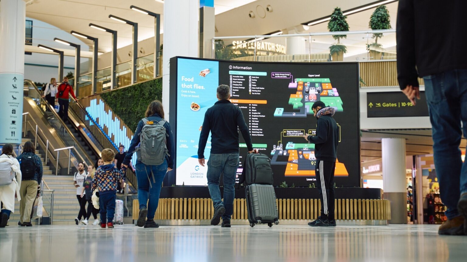 Image shows London Gatwick Airport with screens and passengers with baggage