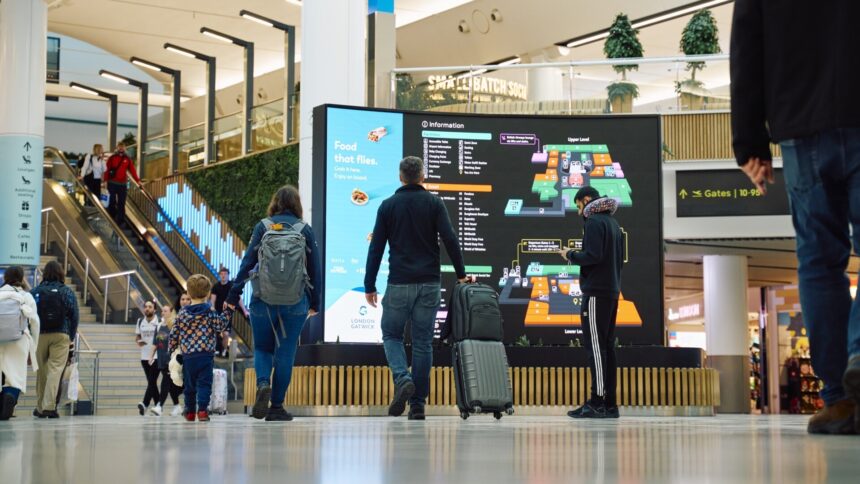 Image shows London Gatwick Airport with screens and passengers with baggage