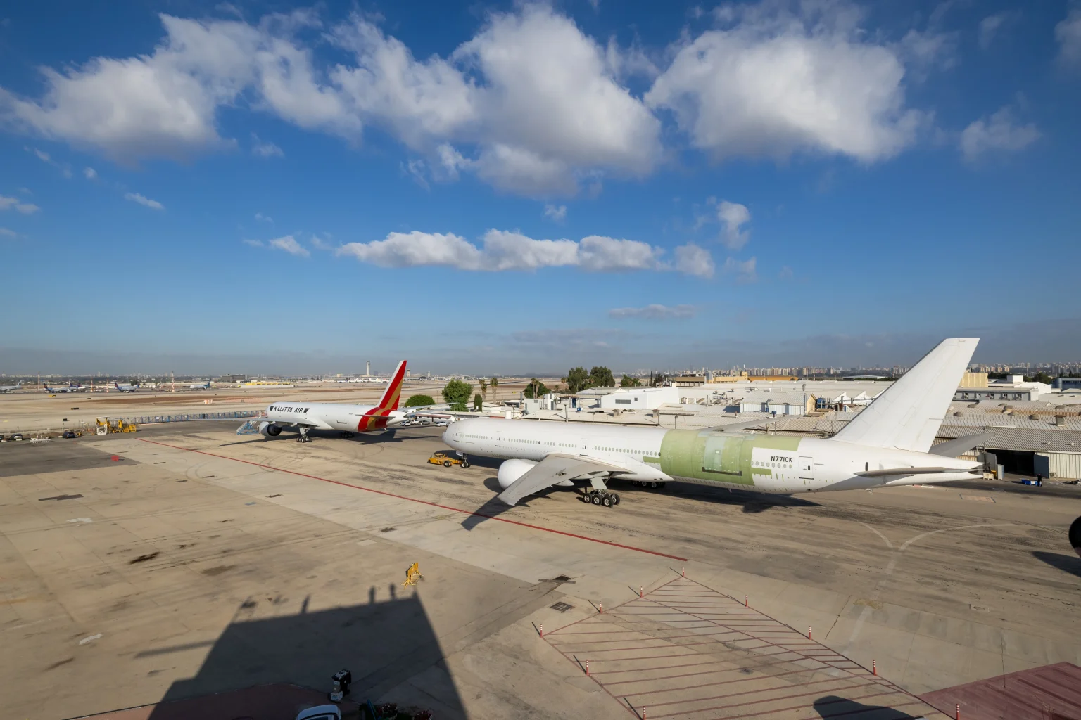 A Kalitta Air Boeing 777 freighter and a second 777 aircraft still in green primer coating, parked on the tarmac at an IAI conversion facility.