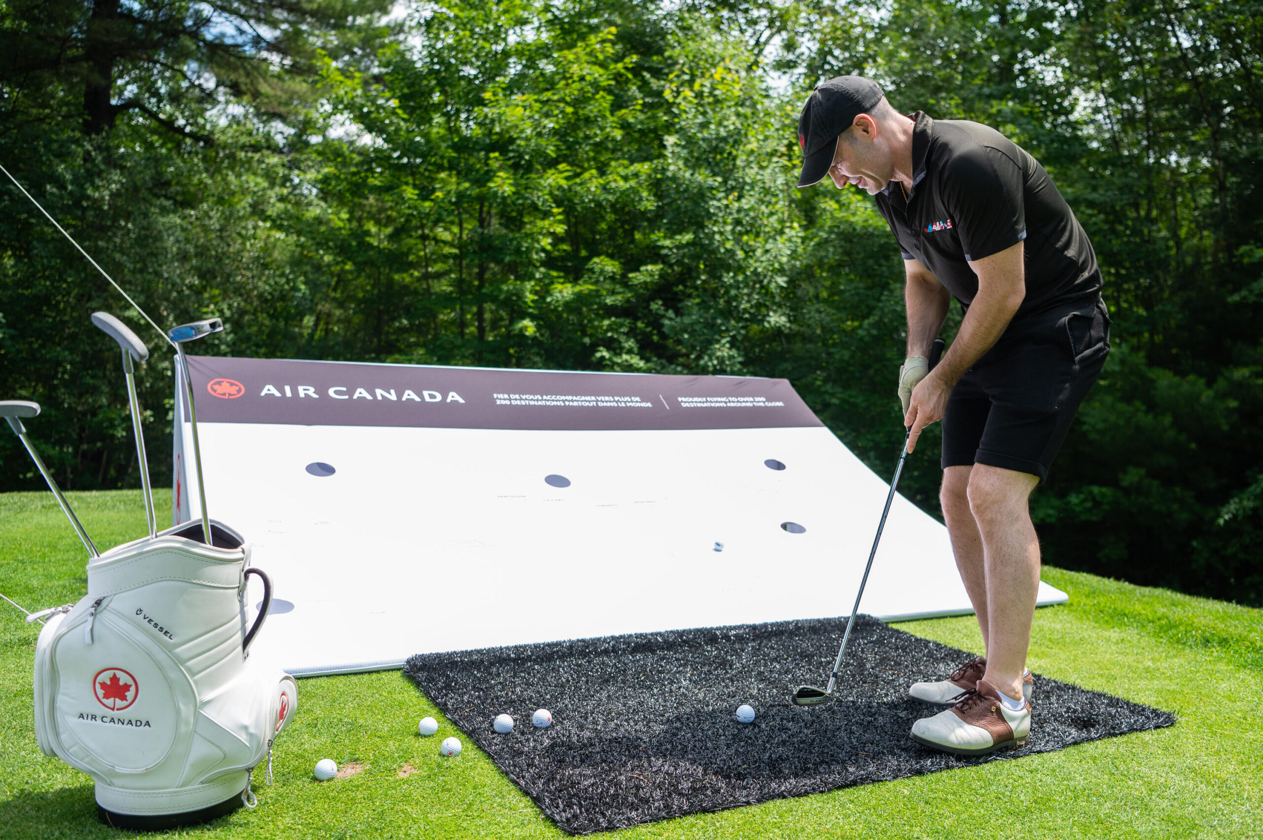 A man putting golf balls into an Air Canada branded hole board, standing on the green with Air Canada branded clubs and club bag.