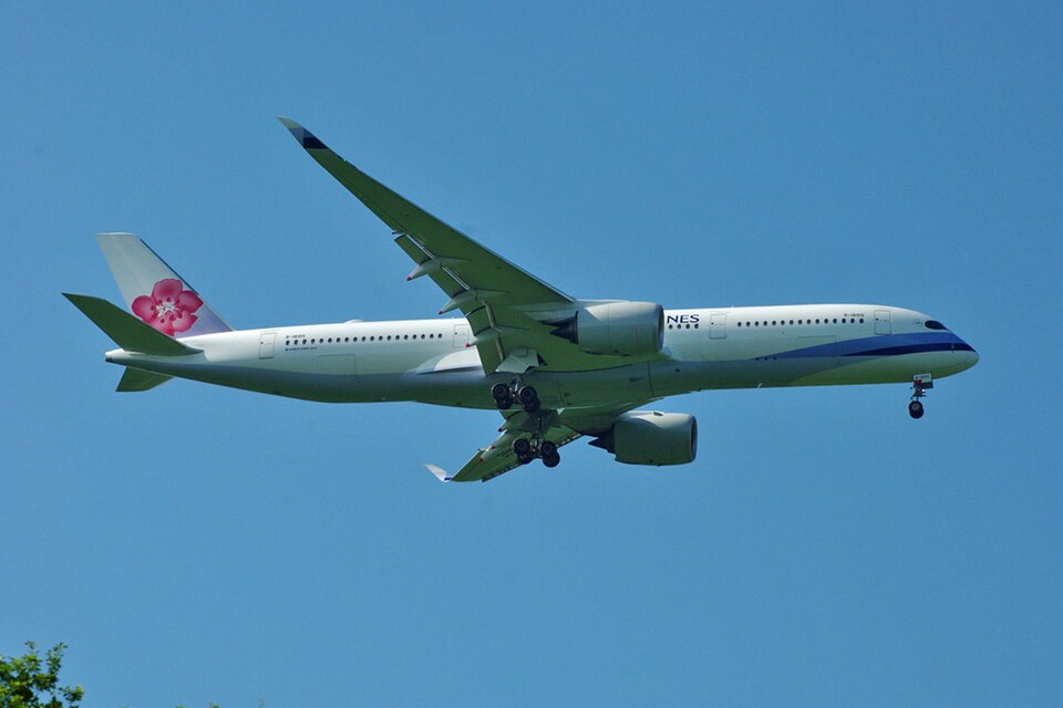 A China Airlines Airbus A350 widebody aircraft flies against a clear blue sky while descending toward London Gatwick Airport. The aircraft's landing gear is fully extended and its flaps are deployed for landing.