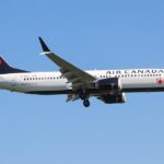 An Air Canada Boeing 737 MAX 8 (registration C-FSJG) on approach with landing gear extended, set against a clear blue sky, showcasing the airline's livery with a white upper fuselage, dark blue belly and tail, and the iconic red maple leaf logo.