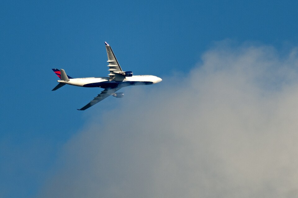 A Delta Air Lines Boeing 767-400ER airliner flying through a blue sky with a large white cloud formation in the background.