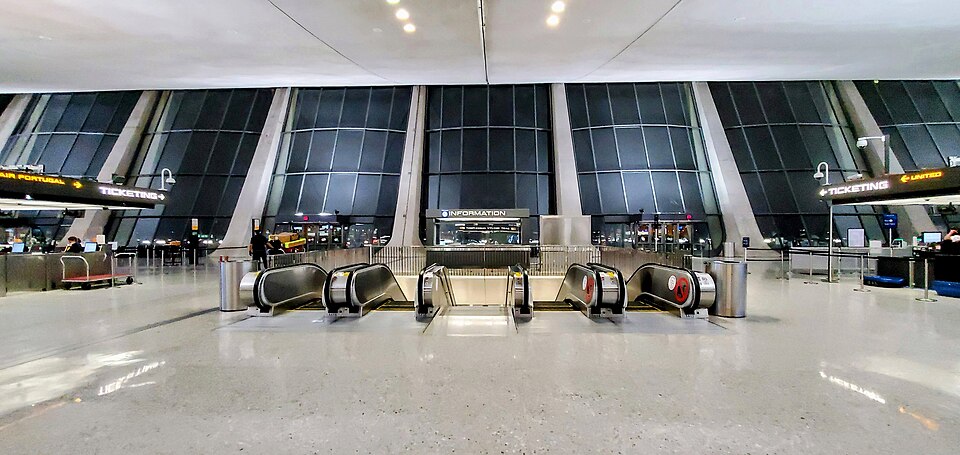 The interior of DUL's main terminal, showing the escalators leading to the departure zones 3 and 4. There are windows from floor to ceiling and the floor is white.