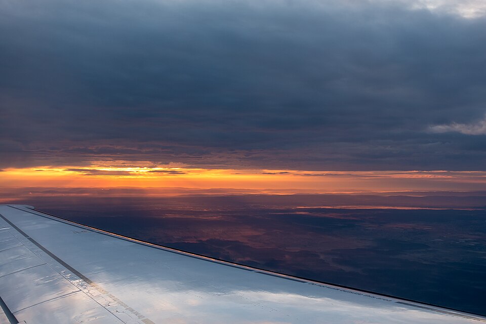 Photo of a colourful blue, yellow and orange sky with the sunsetting over a white plane wing whilst flying over Europe to Berlin