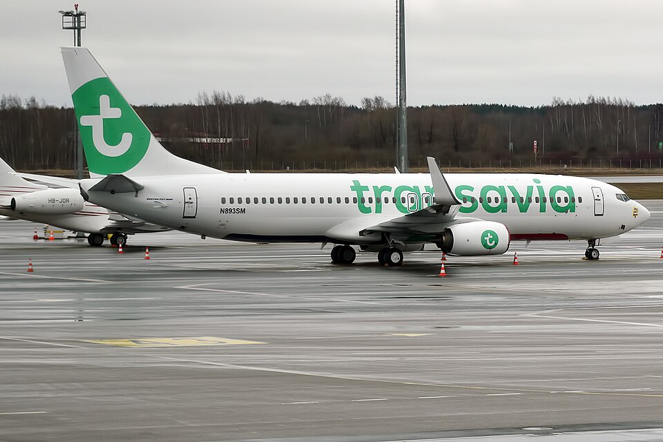 A Transavia Boeing 737-800 is parked on the airport apron in its signature green-and-white livery. The narrowbody aircraft, operated by the Dutch low-cost carrier, is pictured awaiting its next flight with ground equipment positioned nearby
