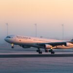 A detailed side-angle view of a four-engine South African Airways Airbus A340-313 commercial jet close to the ground on a runway. The airplane features a white fuselage with "SOUTH AFRICAN" written in dark lettering.