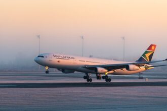 A detailed side-angle view of a four-engine South African Airways Airbus A340-313 commercial jet close to the ground on a runway. The airplane features a white fuselage with "SOUTH AFRICAN" written in dark lettering.