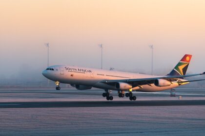 A detailed side-angle view of a four-engine South African Airways Airbus A340-313 commercial jet close to the ground on a runway. The airplane features a white fuselage with "SOUTH AFRICAN" written in dark lettering.