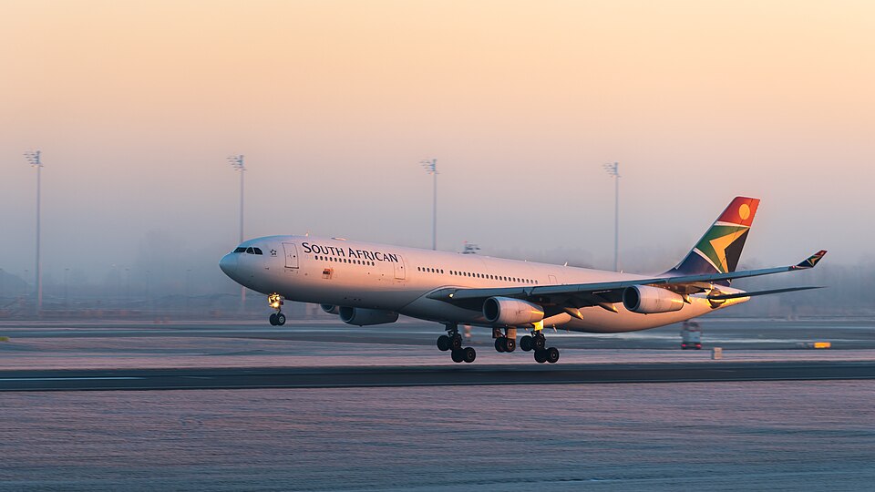 A detailed side-angle view of a four-engine South African Airways Airbus A340-313 commercial jet close to the ground on a runway. The airplane features a white fuselage with "SOUTH AFRICAN" written in dark lettering.