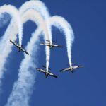 Four propeller planes from The Blades Aerobatic Team perform a synchronised formation dive leaving trails of white smoke against a clear blue sky at the Farnborough Airshow.