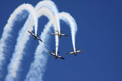 Four propeller planes from The Blades Aerobatic Team perform a synchronised formation dive leaving trails of white smoke against a clear blue sky at the Farnborough Airshow.