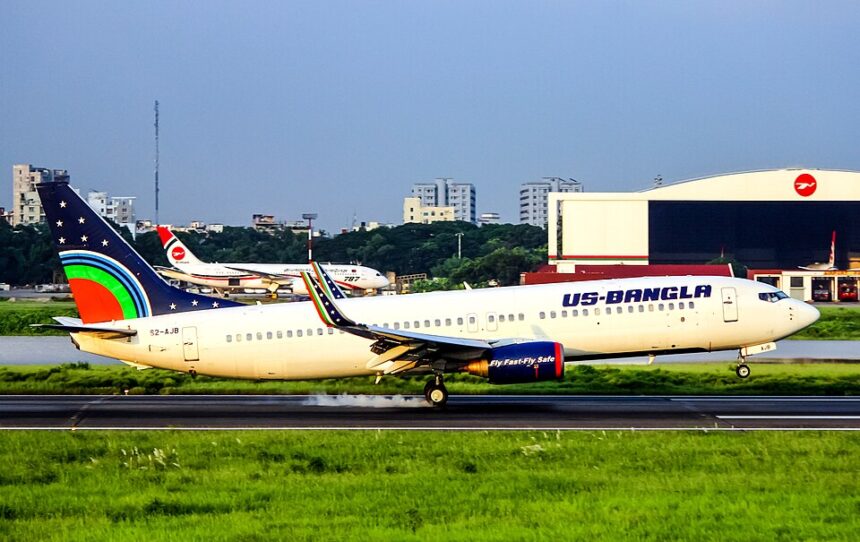 A U.S.-Bangla Airlines Boeing 737 (registration S2-AJB) landing on a runway, with white smoke billowing from its rear tires upon touchdown against a backdrop of green grass and airport buildings.