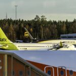 An airBaltic Airbus A220-300 (YL-AAZ) parked on the apron at Stockholm Arlanda Airport (ARN), framed alongside an easyJet fuselage and a UPS cargo jet in the background.