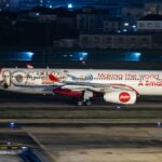 AirAsia X Airbus A330-343, registration 9M-XXF, in 10th anniversary livery reading "Making The World A Smaller Place," landing at night.