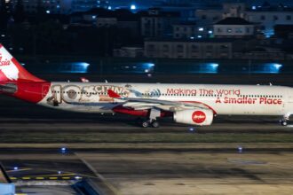 AirAsia X Airbus A330-343, registration 9M-XXF, in 10th anniversary livery reading "Making The World A Smaller Place," landing at night.