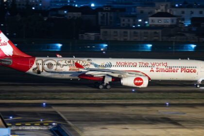 AirAsia X Airbus A330-343, registration 9M-XXF, in 10th anniversary livery reading "Making The World A Smaller Place," landing at night.
