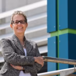Aer Lingus CEO, Lynne Embleton, smiles with her arms crossed, posing beside an Aer Lingus sign.