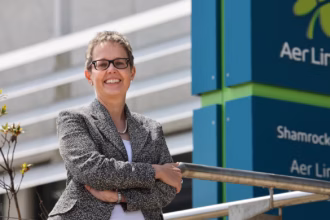 Aer Lingus CEO, Lynne Embleton, smiles with her arms crossed, posing beside an Aer Lingus sign.