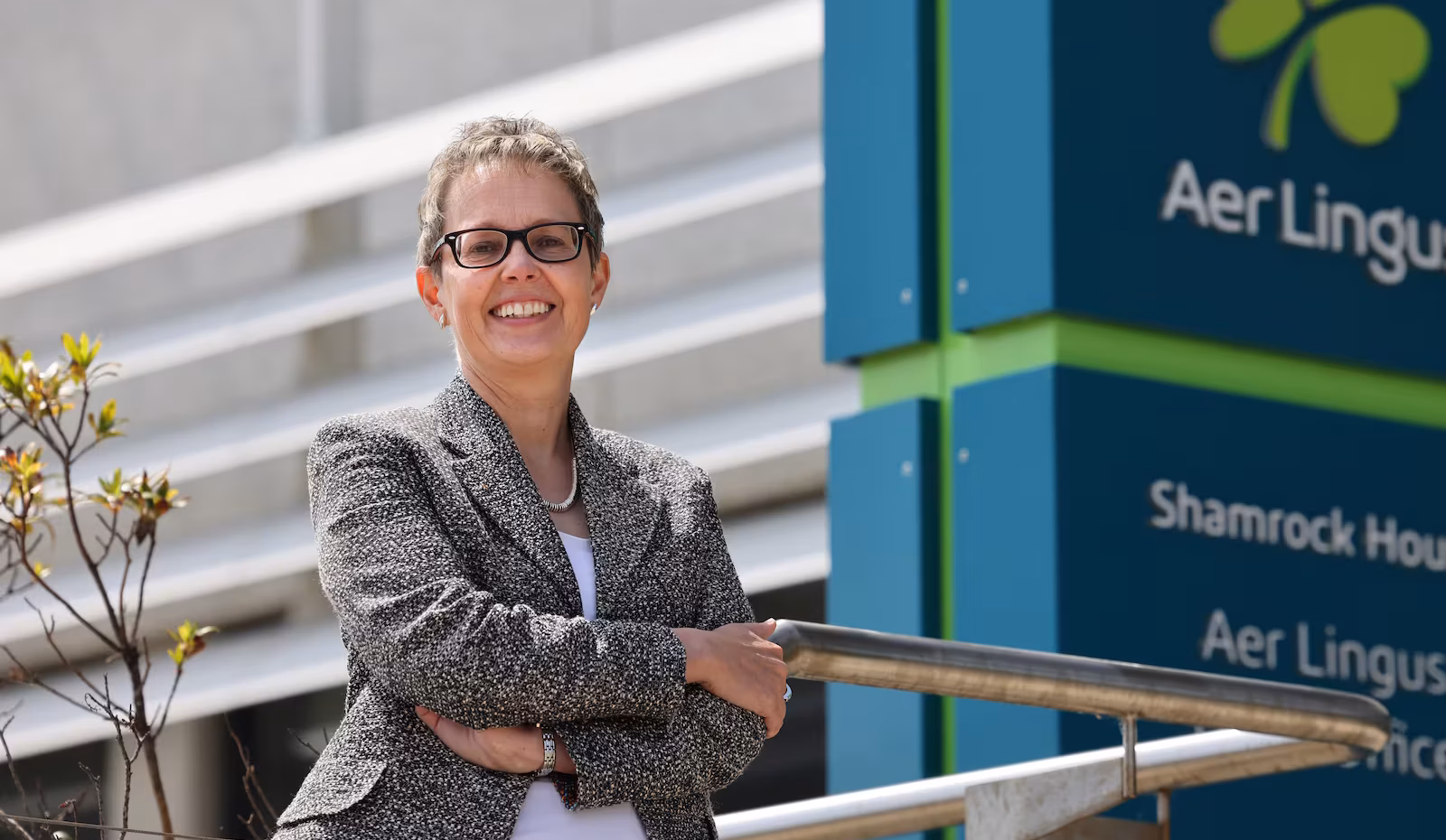 Aer Lingus CEO, Lynne Embleton, smiles with her arms crossed, posing beside an Aer Lingus sign.