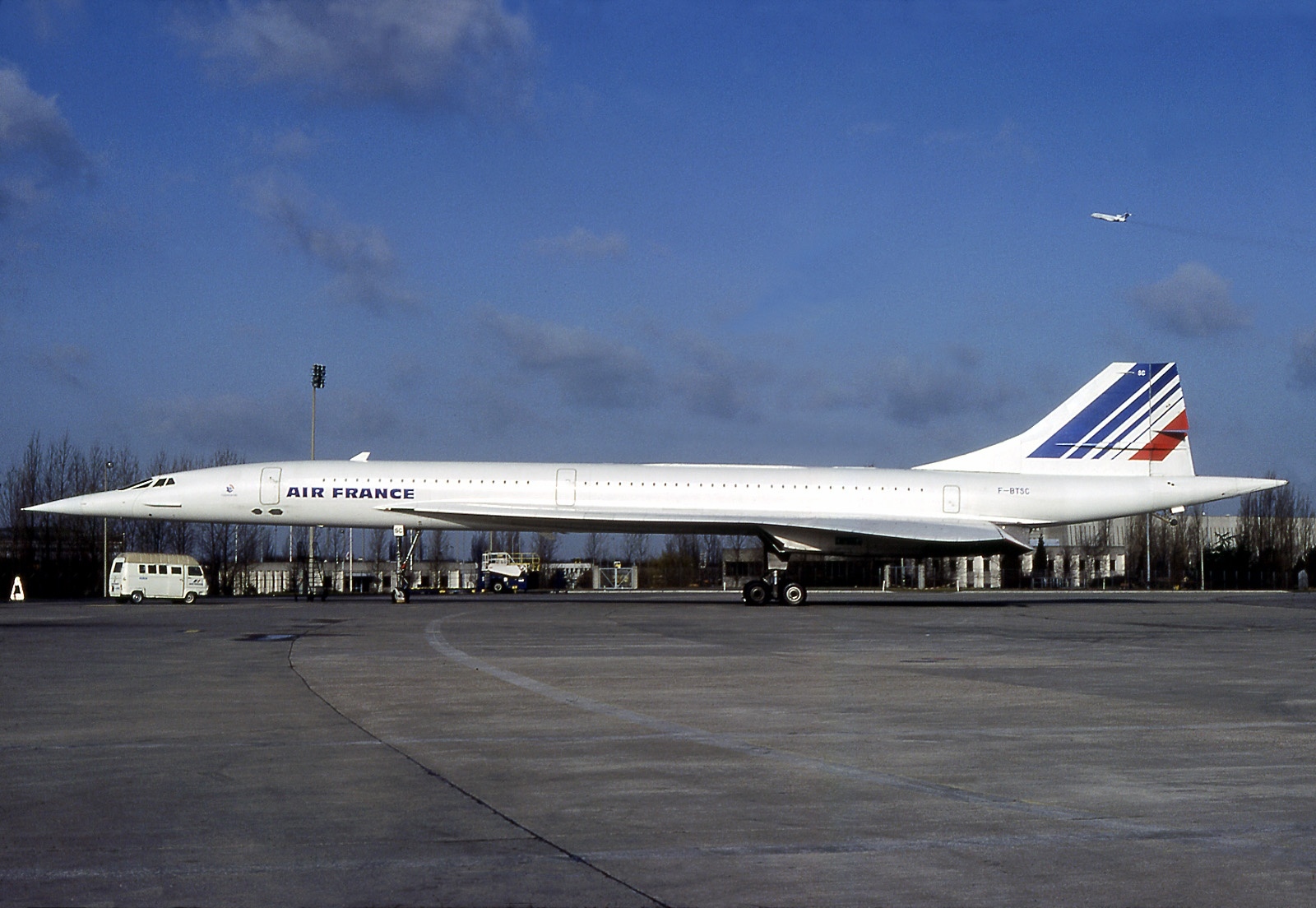 An Air France Concorde pictured on the ground. It is a long pointy white aircraft with 'AIR FRANCE' branding near the front in dark blue, as well as blue white and red striped branding on the tail. The nose is on the centre left and the tail is on the centre right. The background shows blue sky with some clouds.