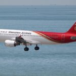 A Shenzhen Airlines Airbus A320 coming in to land with its landing gear out. The sea visible in the background.