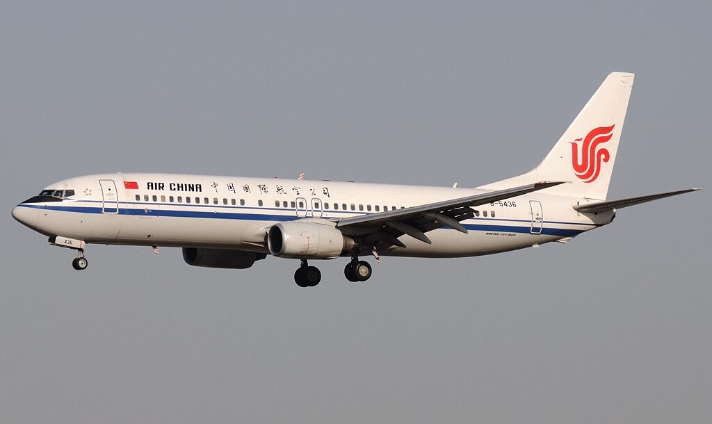 A Boeing 737 Air China aircraft flying in a grey sky. Landing gear is out, coming in to land. Classic white, blue and red livery.