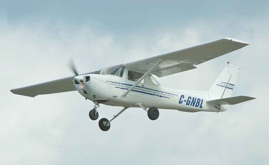 A cessna 150 aircraft flying in the clouds in a white colour wth blue stripes and C-GNBL painted on the side