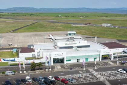 A drone image of the City of Derry Airport (LDY), facing the entrance of the airport. The carpark can be seen at the front, with the runway visible behind the small terminal.