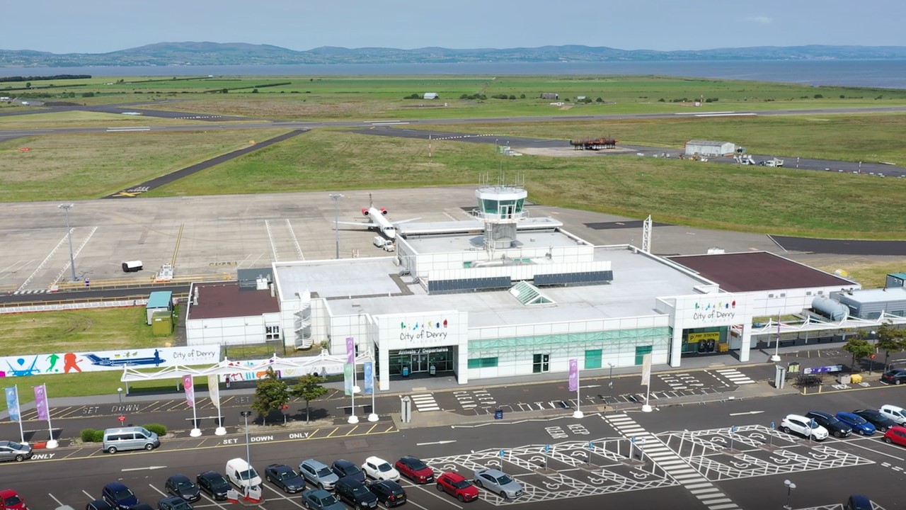A drone image of the City of Derry Airport (LDY), facing the entrance of the airport. The carpark can be seen at the front, with the runway visible behind the small terminal.