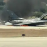 image of the fighter jet crash landed on the runway with smoke and flames coming out from its underside. Emergency response teams heading quickly to the situation.