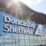 An image showing the entrance of Robin Hood / Doncaster Sheffield Airport (DSA) from the outside. The sun shines against the camera as the blue sky is reflected in the glass facade.
