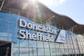 An image showing the entrance of Robin Hood / Doncaster Sheffield Airport (DSA) from the outside. The sun shines against the camera as the blue sky is reflected in the glass facade.