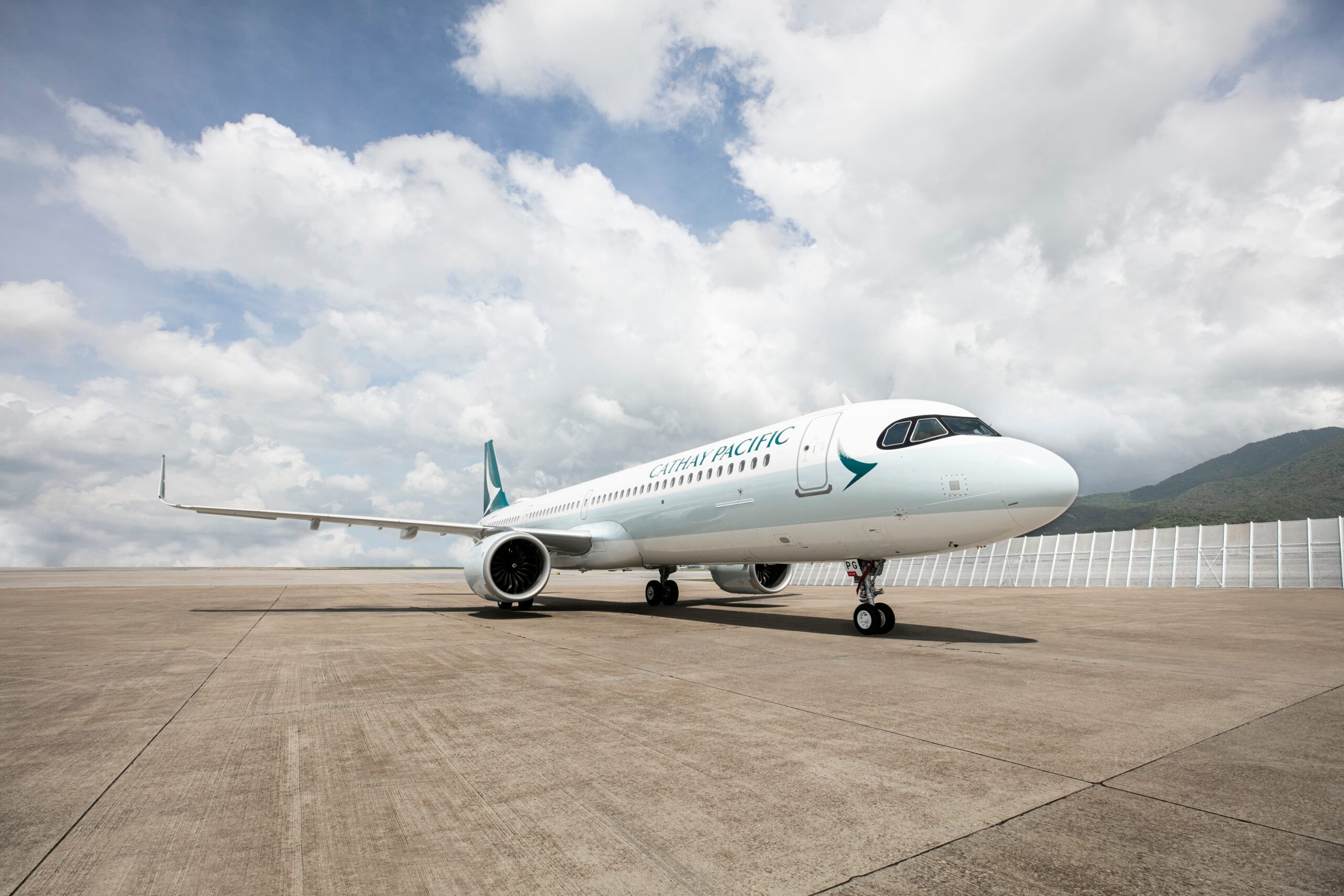 Image shows a grounded Cathay Pacific A321neo aircraft with cloudy sky behind