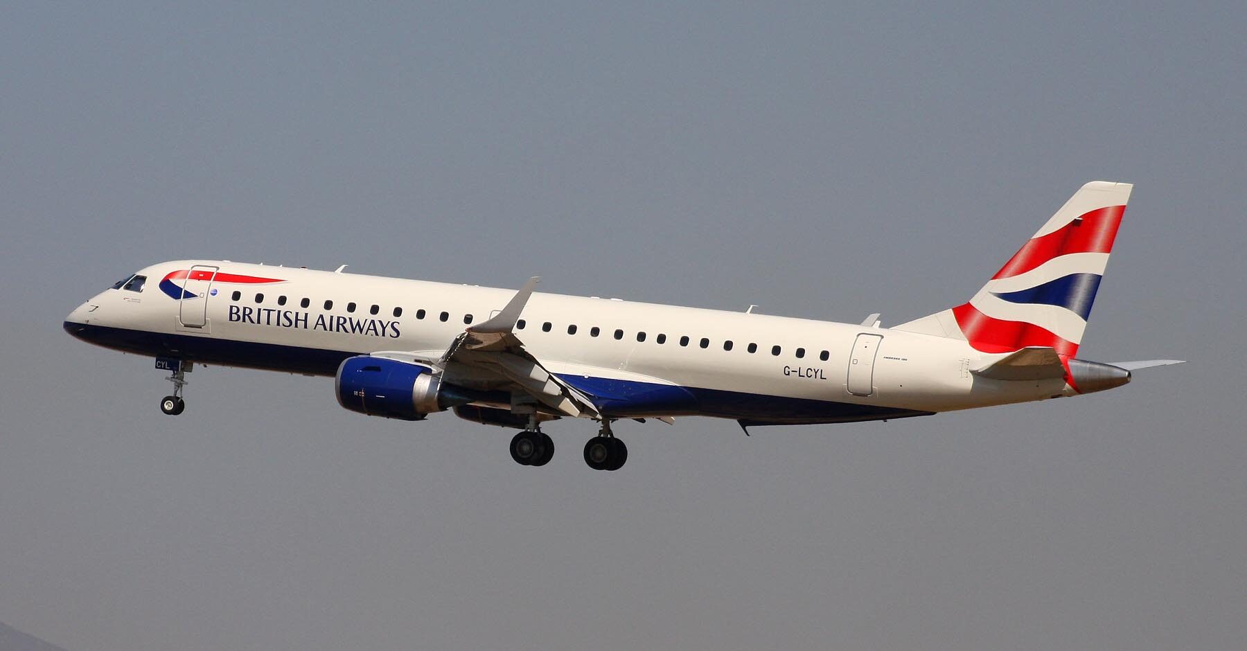A British Airways aircraft flying, with its landing gear still out. Classic white, red and blue livery, against a grey sky.