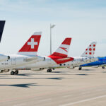 A set of jet tails displaying the logos of some of the Lufthansa Group’s subsidiary airlines. The nets are sat on an airport runway on a cloudy day.