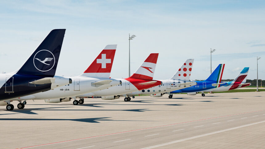 A set of jet tails displaying the logos of some of the Lufthansa Group’s subsidiary airlines. The nets are sat on an airport runway on a cloudy day.