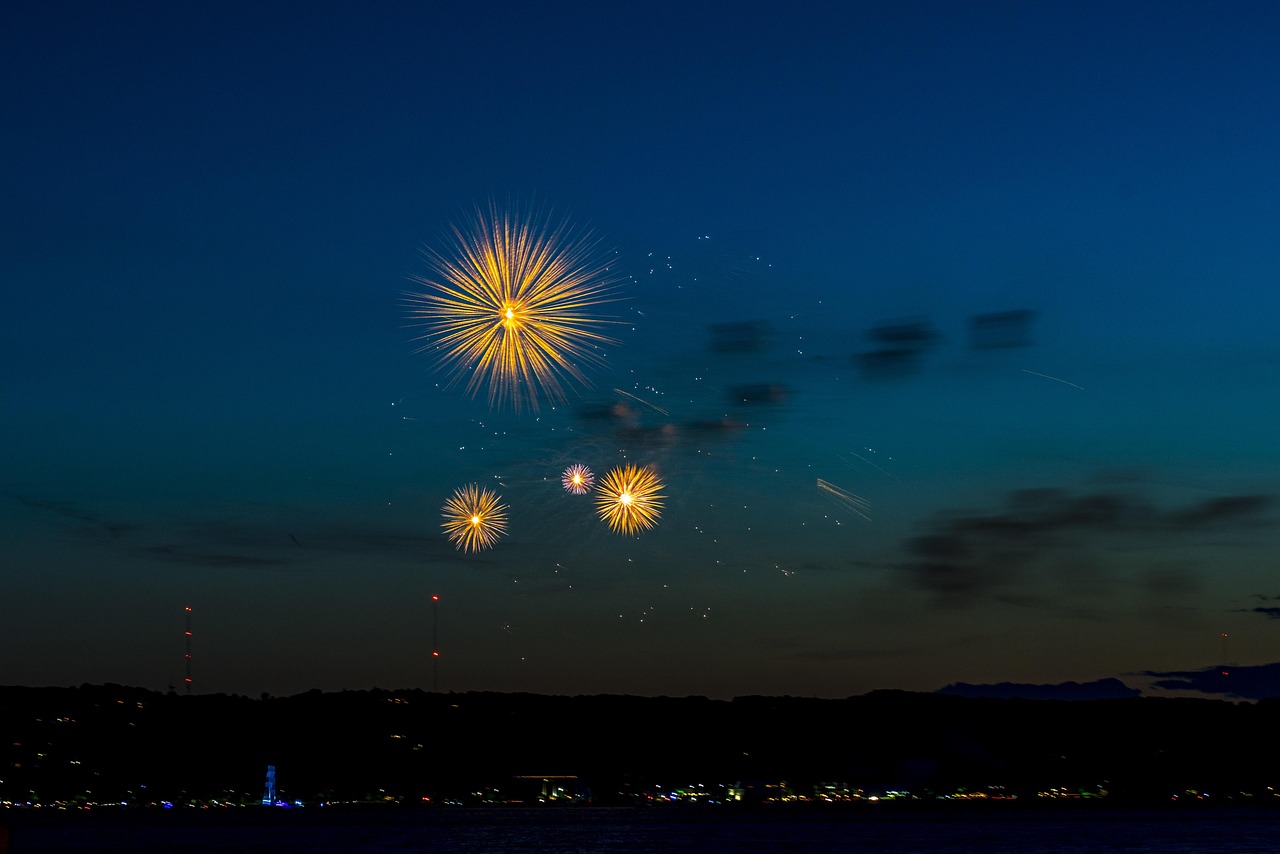 Yellow fireworks in front of a cloudy night sky, with a city skyline visible below.