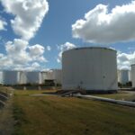 The white oil tanks of the SAF storage terminal in Pinkeba, Brisbane, in the middle of a grass field, in front of a cloudy sky.