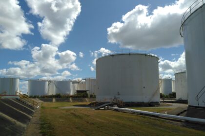 The white oil tanks of the SAF storage terminal in Pinkeba, Brisbane, in the middle of a grass field, in front of a cloudy sky.