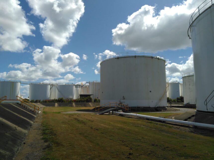 The white oil tanks of the SAF storage terminal in Pinkeba, Brisbane, in the middle of a grass field, in front of a cloudy sky.